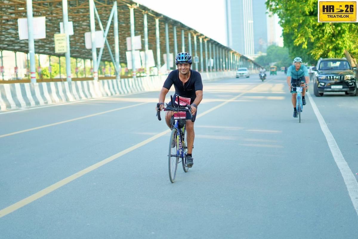 Vivek Sharma on the bike at HR26 Duathlon, smiling on a bridge